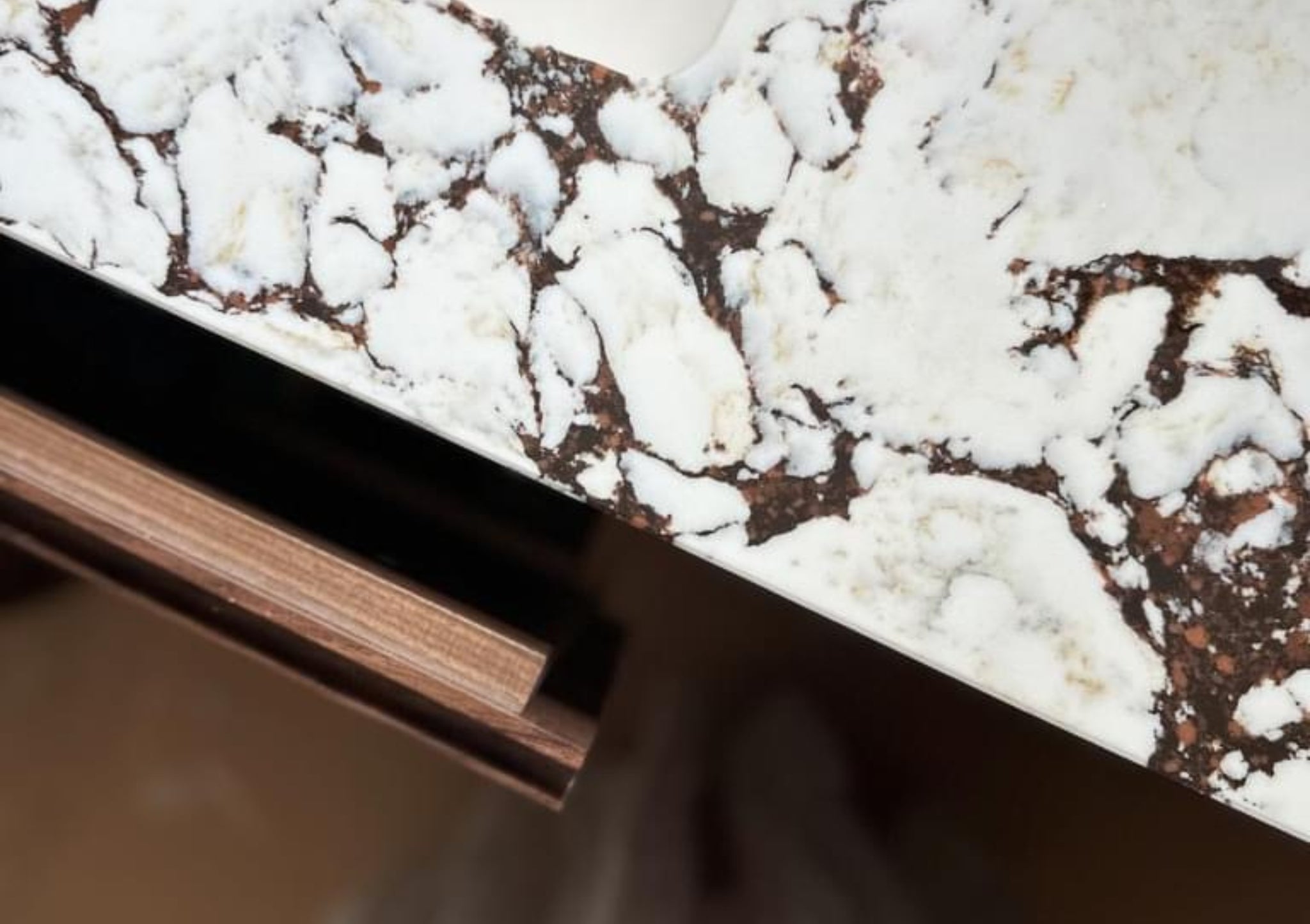 Close up image of a kitchen counter with brown and white marble worktop and wooden drawer